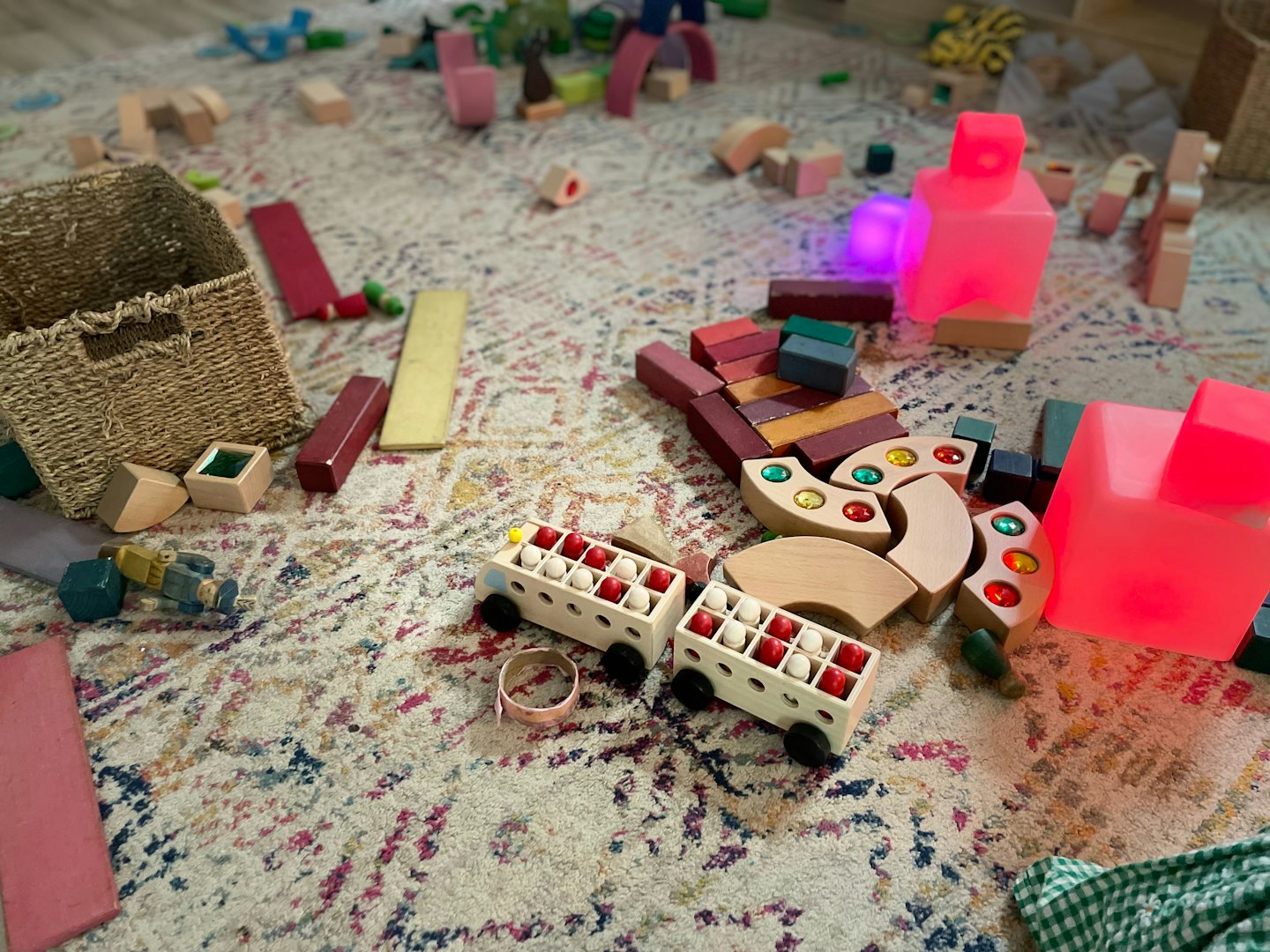 Childrens wooden blocks and toy cars scattered on a rug.