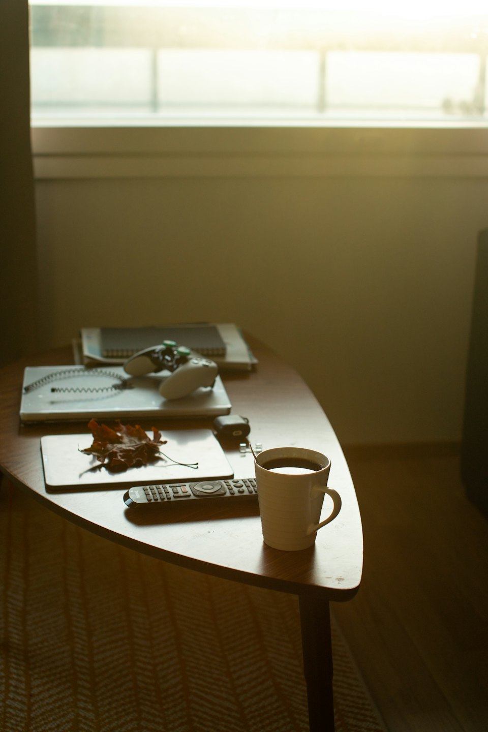 Wooden table with coffee, remote, leaf, and game controller.